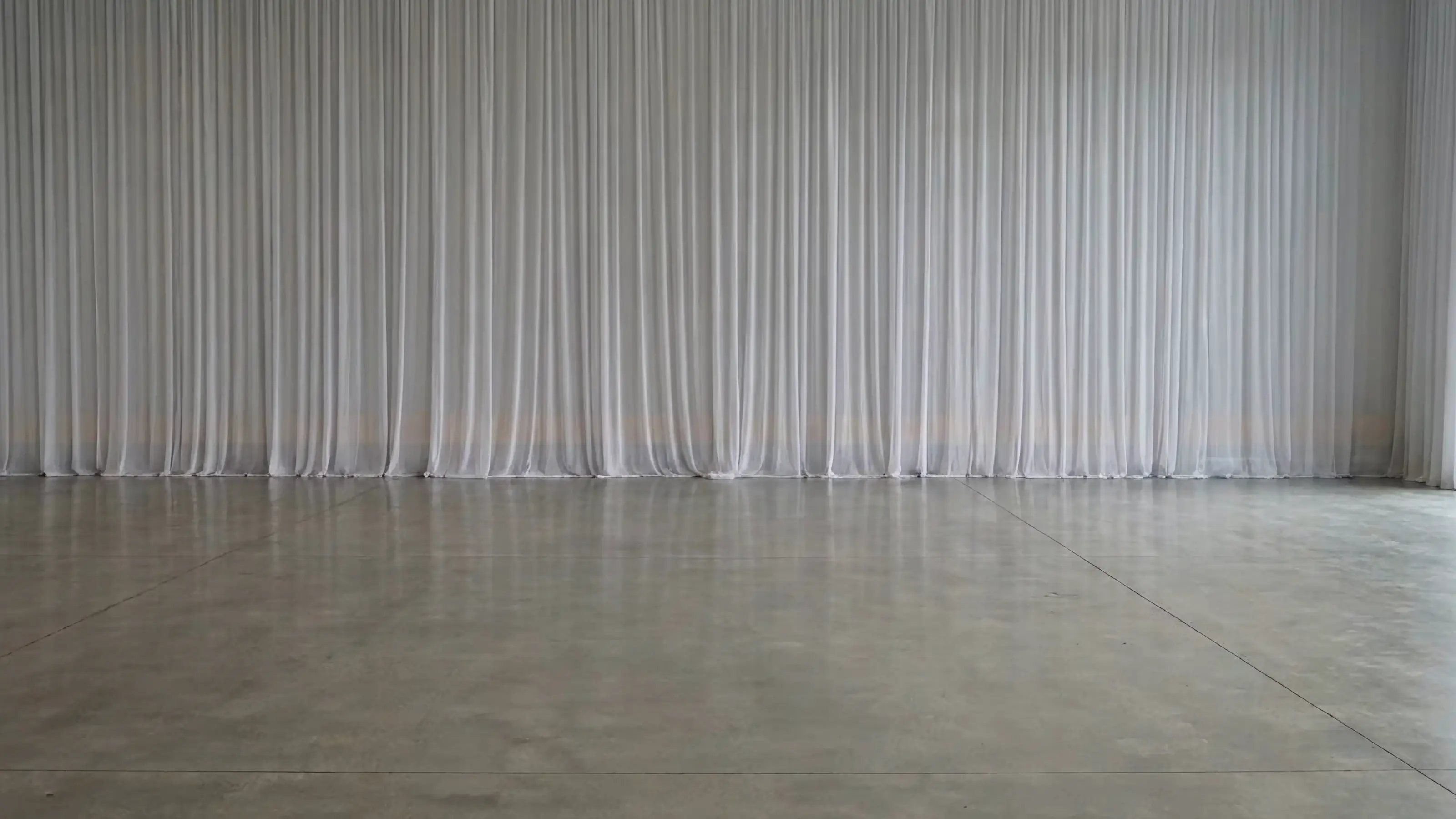 An empty hall: white drapes along the far wall above a bare concrete floor.